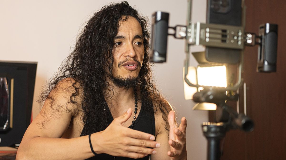 A performer talking to a camera on a tripod with an LED panel beside it, filming indoors